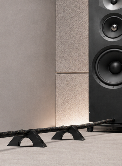 Speaker cable elevated above the floor by Cable Arch supports near a loudspeaker in a listening room.