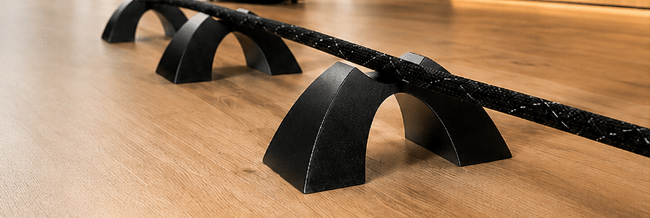 Black Cable Arch speaker cable support elevating a braided speaker cable above a wood floor.